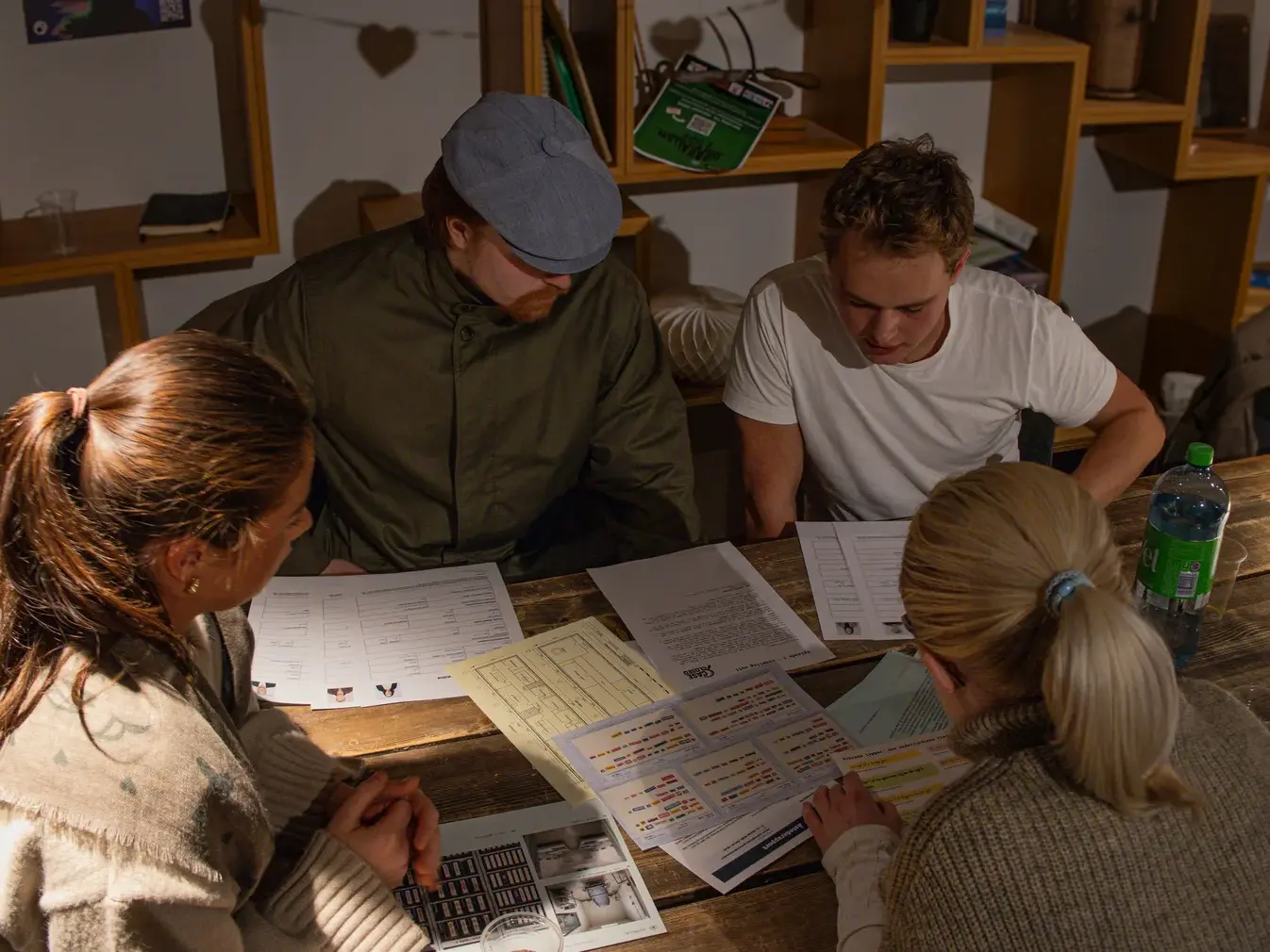Fire spillere rundt et bord med plantegninger, avhør og skjemaer, to av dem peker i dokumentene.