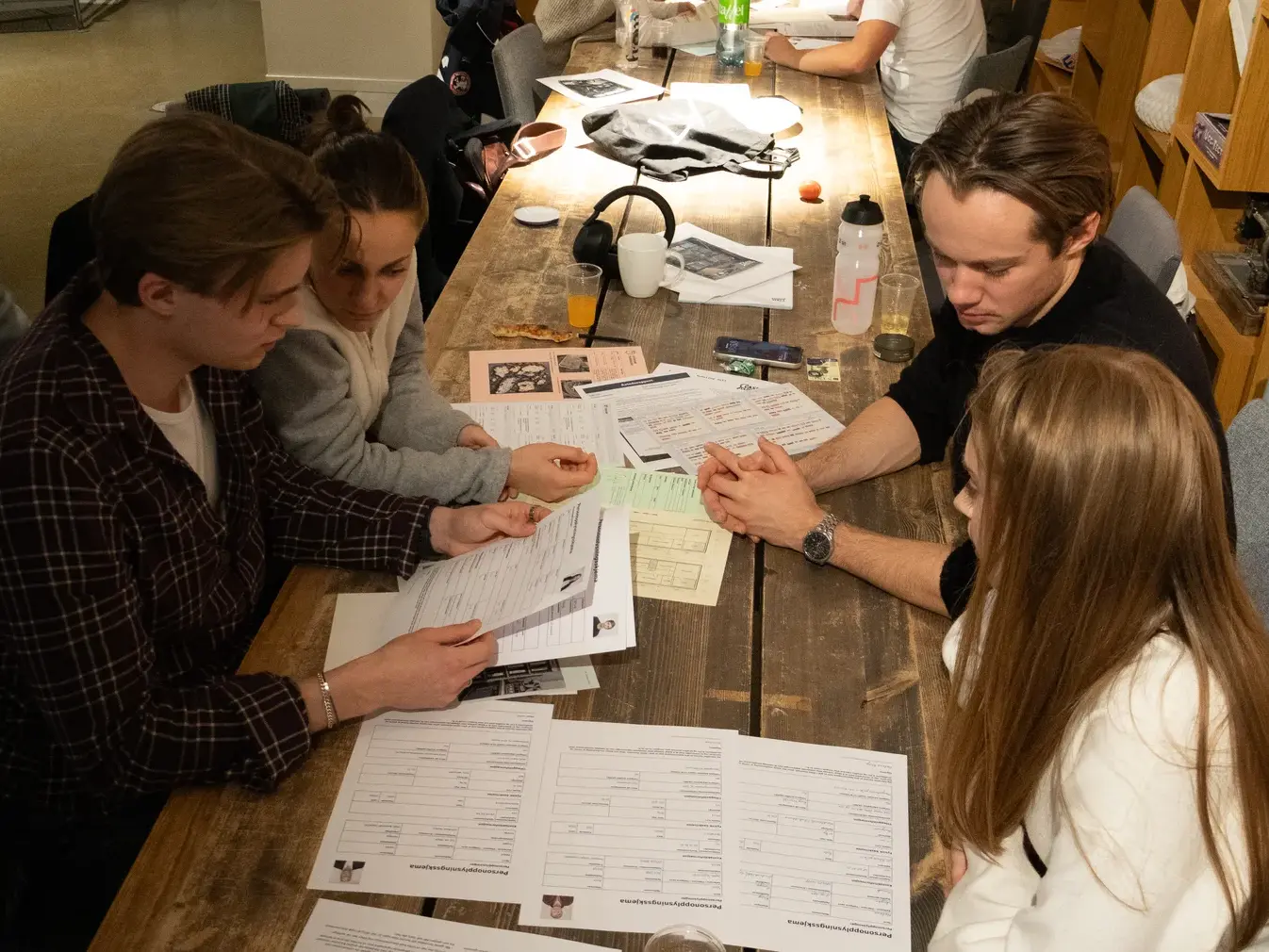 Fire spillere ved et langbord går gjennom personopplysningsskjemaer og en plantegning.